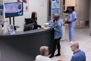 Young adult filling in registration form at hospital reception desk, writing medical checkup report before attending appointment. Woman checking papers in facility lobby, having consultation.